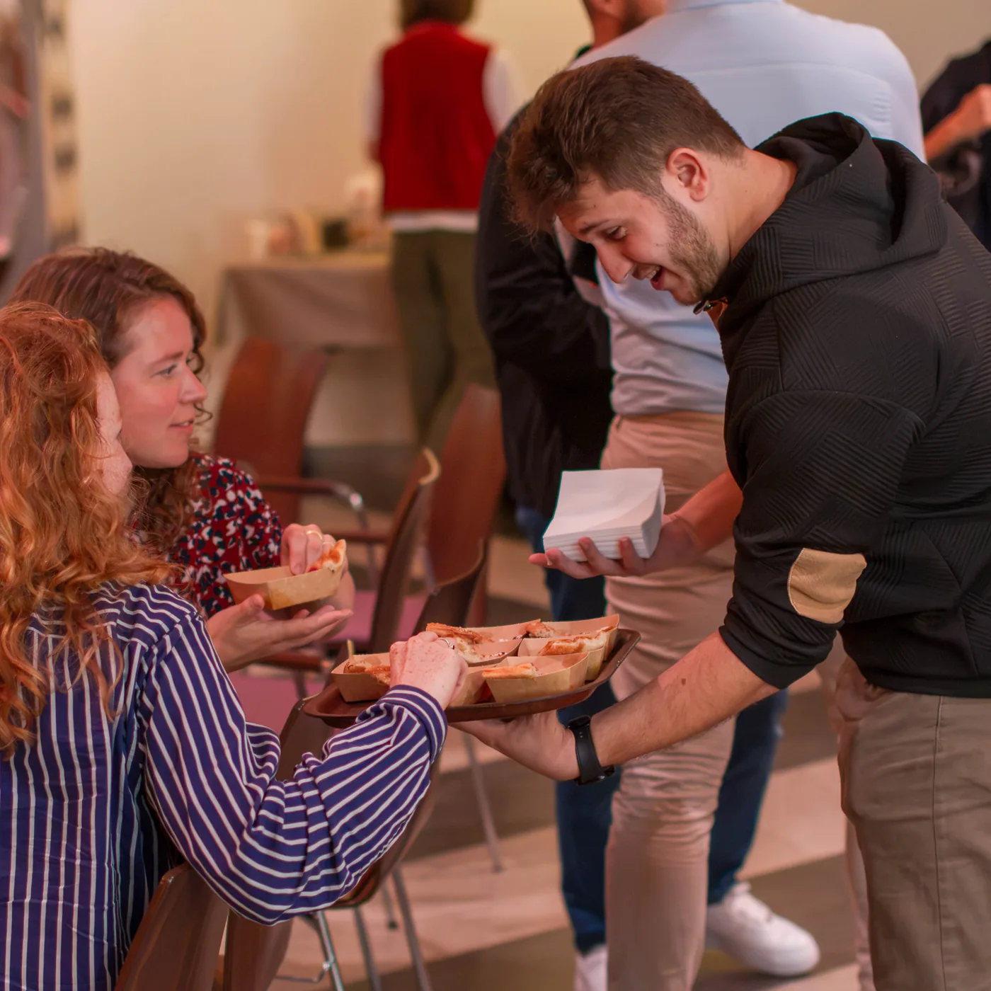 Een jonge man biedt deelnemers een schaal met hapjes aan.