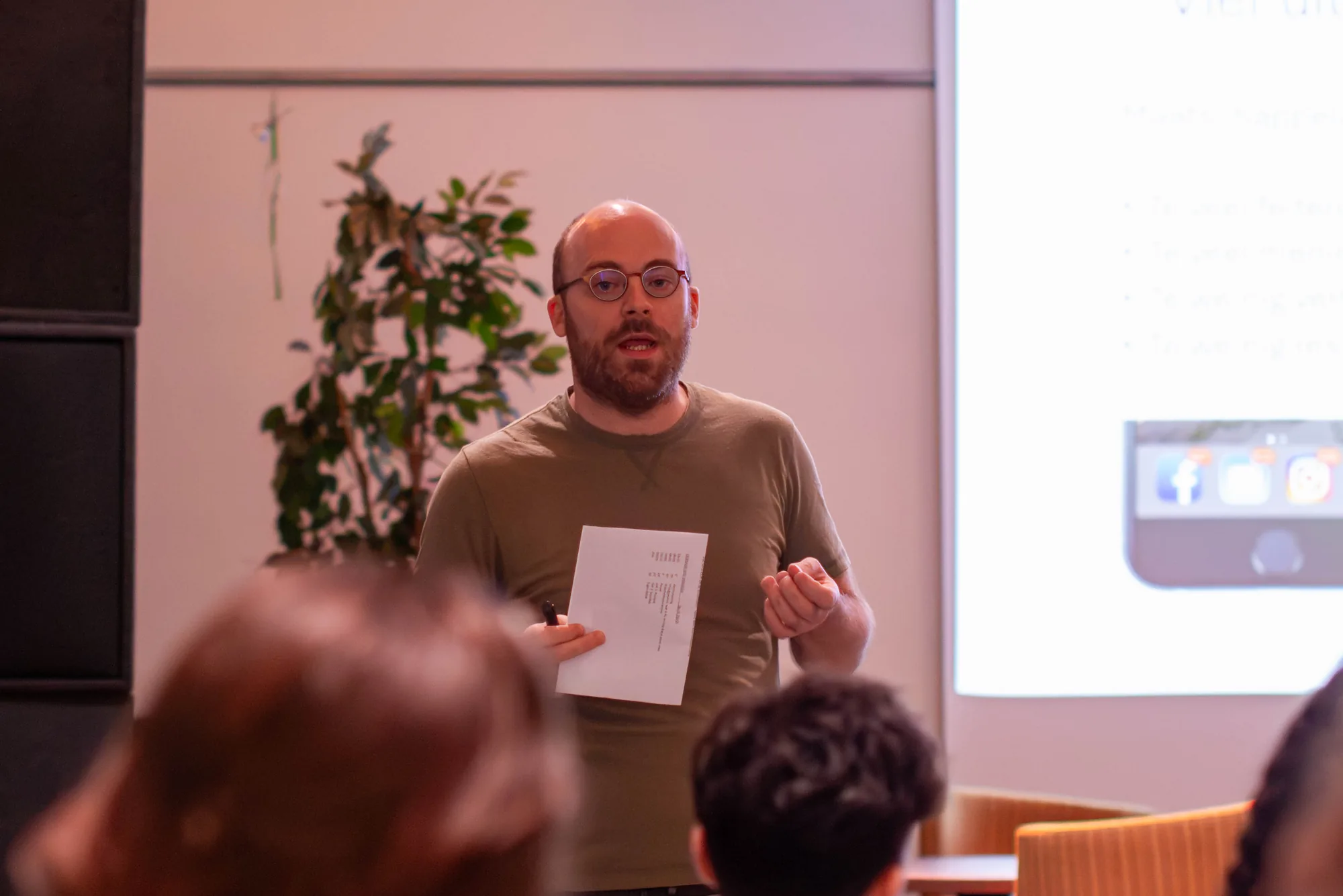 Cultuurfilosoof Simon Truwant spreekt het publiek toe tijdens de bijeenkomst bij Argan, naast een projectiescherm met zijn presentatie.